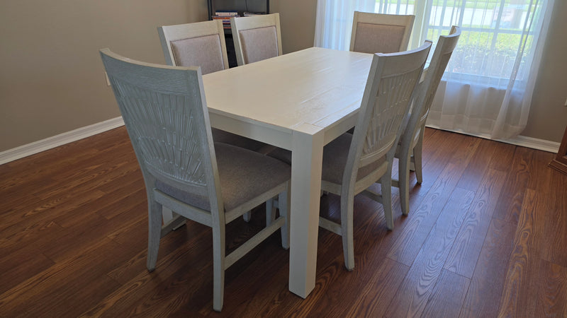 White dining table with six chairs on a wooden floor