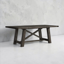 Wooden dining table with X-shaped legs against a concrete wall.