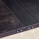 Close-up of a dark wooden door with metal hardware on a concrete floor.
