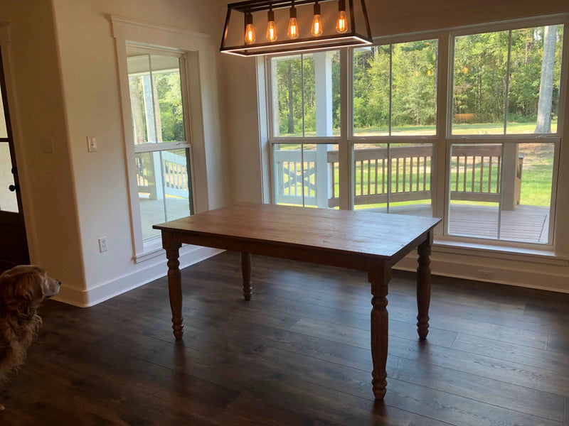 Wooden dining table in a room with large windows showing a green outdoor view.